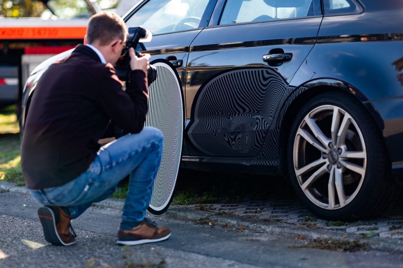 Ein Mann fotografiert ein schwarzes Auto, während er kniet und einen Reflektor hält.